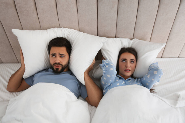 Young couple suffering from noisy neighbours in bed at home, above view - Foto, imagen