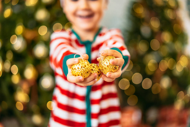 Egy kisfiú kezei karácsonyi játékokkal egy karácsonyfa hátterében. az ünnep fogalma. - Fotó, kép