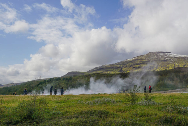 Haukadalur, IJsland: Bezoekers wachten tot de actieve Strokkur geiser uitbarst. Het stuurt om de paar minuten waterstralen en stoom de lucht in.. - Foto, afbeelding
