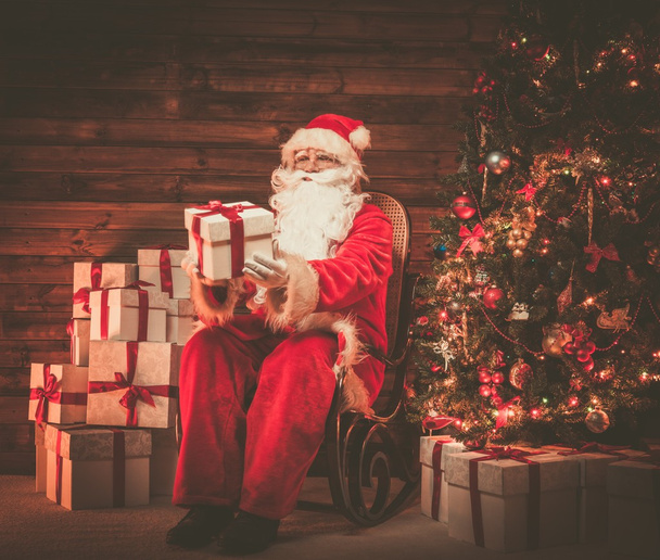 Santa claus siedzi na bujanym fotelu w drewnianym domu wnętrza prezentacji ozdobne pudełko - Zdjęcie, obraz