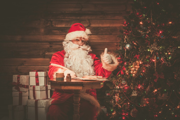 Weihnachtsmann im hölzernen Hausinneren sitzt hinter Tisch und schreibt Briefe mit Federkiel - Foto, Bild
