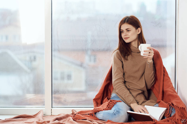 woman with a cup of drink on the windowsill reading a book rest morning - Foto, immagini