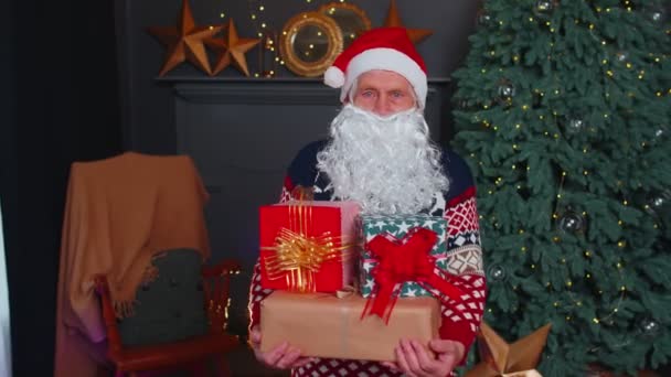 Abuelo mayor parodia a Papá Noel presentando caja de regalo de Navidad, celebración de fiestas en casa - Imágenes, Vídeo