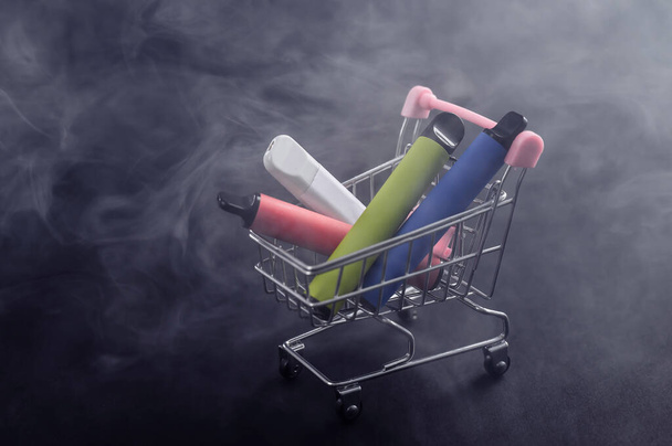 Disposable vapes in a shopping cart on a black background. Modern electronic cigarettes. - Fotografie, Obrázek
