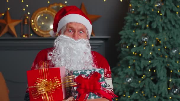 Senior grandfather parodies Santa Claus presenting Christmas gift box, holidays celebration at home - Footage, Video