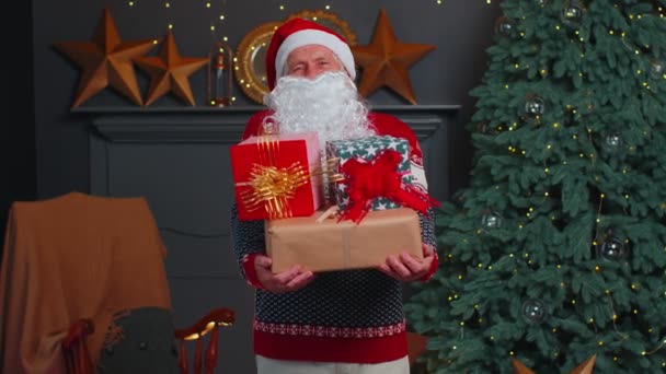 Senior grandfather parodies Santa Claus presenting Christmas gift box, holidays celebration at home - Footage, Video