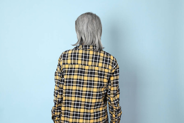 The senior Asian man with yellow plaid shirt standing on the blue background. - Photo, Image