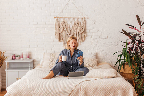 Beautiful young woman in pajamas, working on a laptop in bed, talking on the phone. Online shopping - Foto, Bild