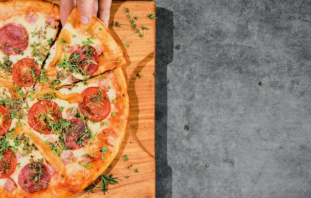 Pizza met mazzarella kaas, peperoni en tomaten op grijze achtergrond, meisjeshand neemt plak pizza. Pizzeria reclame poster concept met heerlijke pizza. Indeling met vrije ruimte voor tekst - Foto, afbeelding