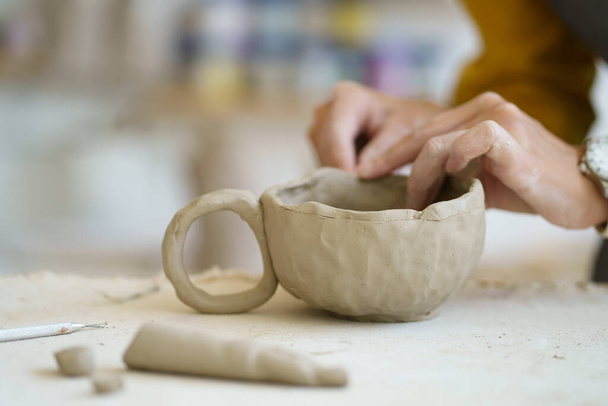 Terapia plastyczna na lekcji ceramiki: kobiece dłonie kształtujące kubek garncarski. Artysta pracuje z surową gliną w studio - Zdjęcie, obraz
