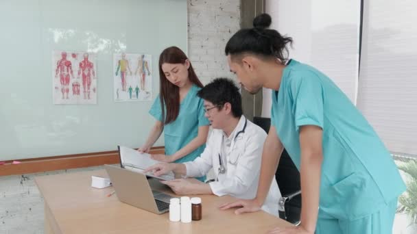 Az egészségügyi csapatmunka egy csoportja. Három fiatal felnőtt egyenruhás ázsiai etnikai orvos gyógyszerekről tárgyal a kórház rendelőjében. A szakemberek szakértők és szakemberek.. - Felvétel, videó