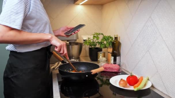 Woman cooking sauce bolognese and use smartphone - Footage, Video