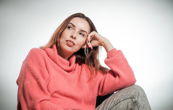 young thinking woman portrait in pink sweater on studio background - Фото, изображение