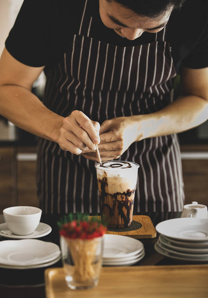 Barista dekoriert sorgfältig cremigen Schaum aus Eiskaffee, indem er mit einem Zahnstocher Schokoladenmuster wie ein Spinnennetz darauf zeichnet, damit es zum Trinken attraktiver aussieht. - Foto, Bild