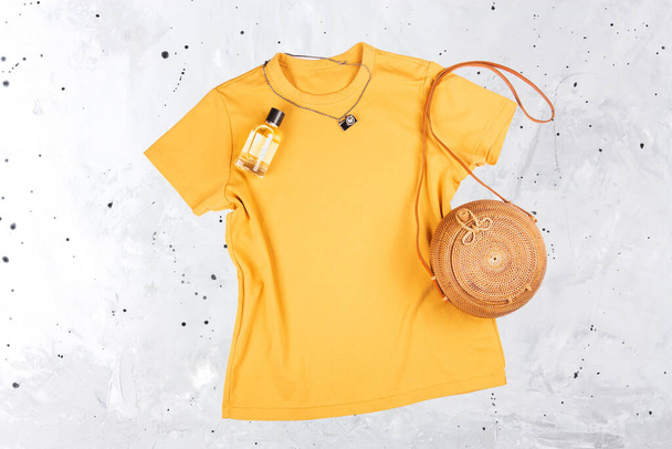 Λευκό κίτρινο γυναικείο t-shirt mockup σε γκρι φόντο με ψάθινη τσάντα. - Φωτογραφία, εικόνα