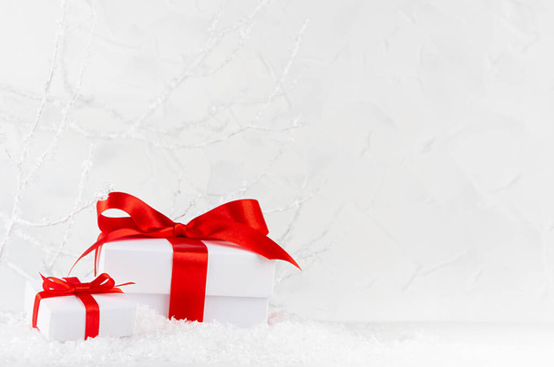 Two bright christmas present boxes with red bow in white decorative winter forest with snow, frosty branches, copy space. Holiday New Year background for design. - Φωτογραφία, εικόνα
