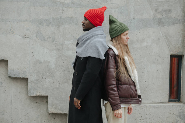 Longshot of standing back to back opposite sex friends out on the street. Both dressed warmly for late autumn. Wearing same fashion knitted hats. - Foto, imagen