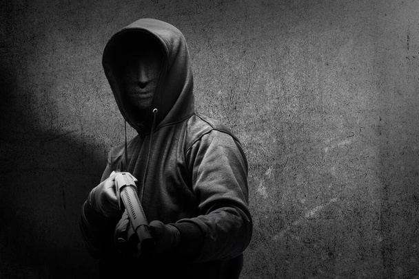 Criminal man in a hidden mask holding the shotgun with black wall background - Valokuva, kuva