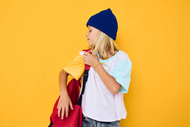 girl in a hat with a backpack school yellow background - Photo, Image