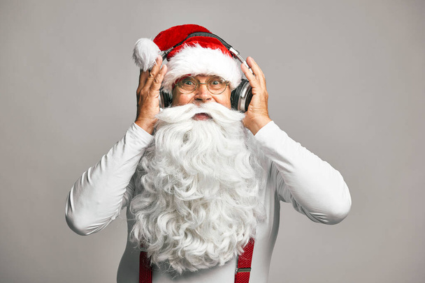 Valkoihoinen joulupukki harmaalla taustalla yllään kuulokkeet asetettu - Valokuva, kuva