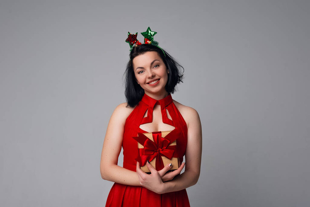 Young woman portrait hold gift in christmas color style, wearing red dress. Smiling happy girl on white background - Foto, immagini