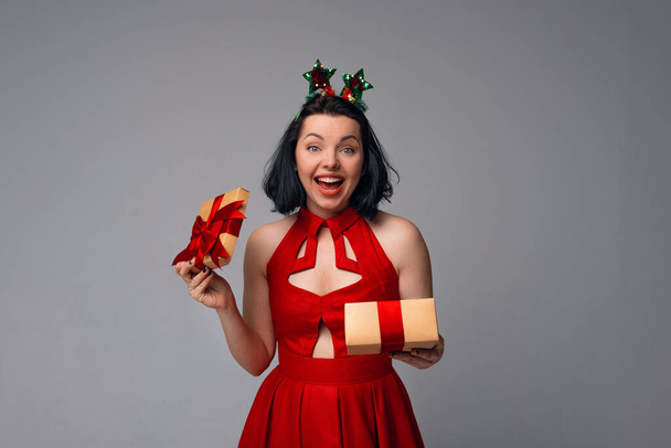 Portrait of a Young Woman opening gift box and looking at camera with a happy smile on face, standing over gray background. Holidays, celebration and lifestyle concept - Photo, Image