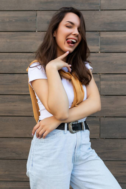 Vertikální fotografie sexy docela atraktivní krásné usměvavý šťastný pozitivní okouzlující mladá brunetka mladá žena na sobě stylové oblečení: bílé tričko a světle modré džíny na ulici ve městě v blízkosti - Fotografie, Obrázek