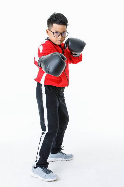 Lovely cutout portrait of smart young healthy Asian boy wearing red jacket, black pants, and boxer gloves standing tight and ready to fight strongly with happily smiling as enjoy boxing practice - Zdjęcie, obraz