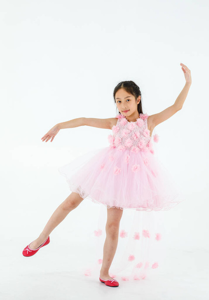 Izolované celé tělo studio záběr na malý roztomilý pěkný asijské balerína dítě nosí růžové krásné růže květiny baletní šaty a červené boty s úsměvem pózuje šťastně tančit před bílým pozadím. - Fotografie, Obrázek
