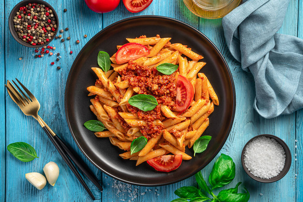 Penne pasta with bolognese sauce on a blue background. Italian cuisine. Top view, close-up. - Photo, Image