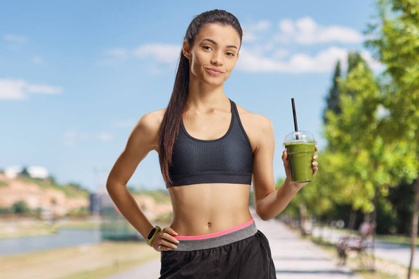 Young female in crop top holding a green smoothie outdoors - Fotó, kép