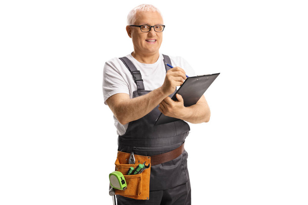 Repairman with a tool belt writing a document on a clipboard isolated on white background - Foto, Bild