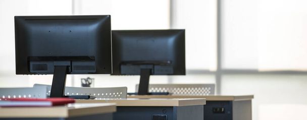 Hintergrundbild eines modernen Innenraums, Büros oder Arbeitsplatzes mit niemandem und einer Reihe von Computern auf hölzernen Schreibtischen oder Tischen. Technologie und Geschäftskonzept - Foto, Bild