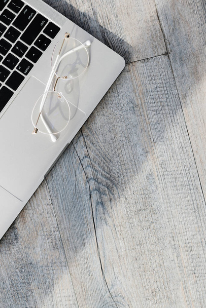 Close-up bovenaanzicht opname van witte optische bril bij een pauze rust ontspannen geplaatst op computer laptop toetsenbord naast sappige plant pot op oude houten textuur tafel met lege kopieerruimte. - Foto, afbeelding