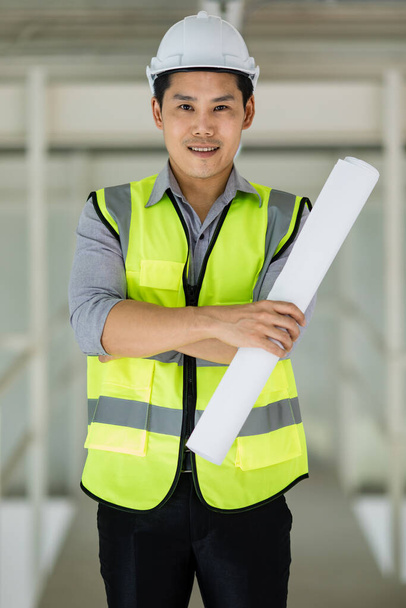 Beau jeune ingénieur asiatique en gilet réfléchissant jaune et portant un casque de sécurité travaillant dans le site de construction. - Photo, image