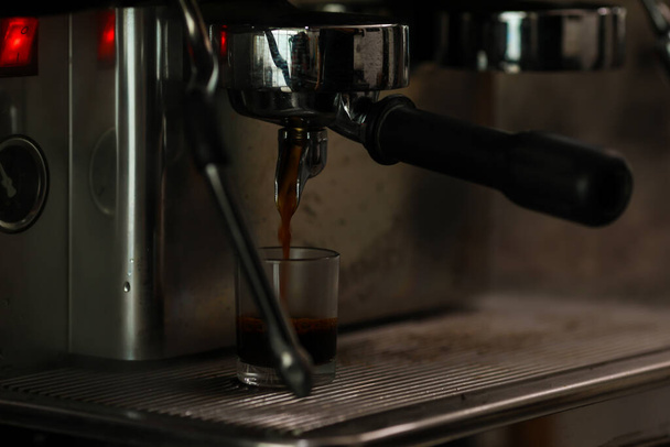 Close up shot of measuring glass filling with dark brown hot delicious good smell coffee by luxury clean steel coffee making machine in cafe with blurred background. - Фото, зображення
