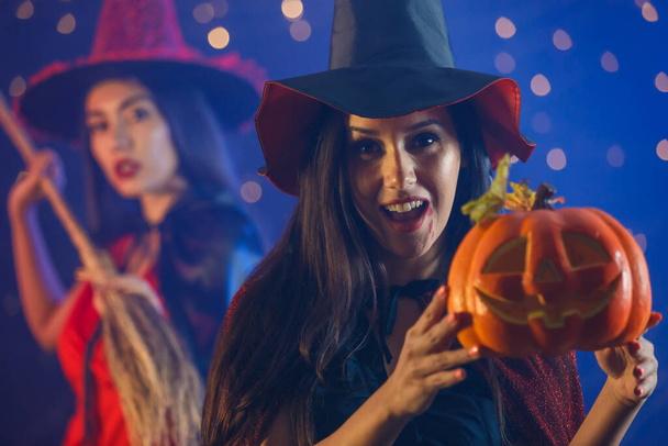 Jovem mulher em roupa de bruxa demonstrando Jack O Lantern enquanto se diverte durante a festa de Halloween com o amigo - Foto, Imagem