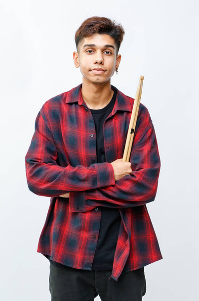 Portret przystojnego młodego perkusisty, który krzyżuje ramiona i trzyma w studio pałeczki perkusyjne. Młody, modny młodszy muzyk stojący z talerzem i patrzący w kamerę z białym tłem - Zdjęcie, obraz