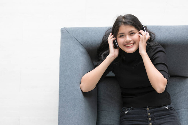 Bird-eye view retrato de jovem adolescente tailandês-turco gosta de ouvir música com fone de ouvido e mãos toque gesto fone de ouvido. Menina júnior deitada no sofá cinza isolado com fundo branco - Foto, Imagem
