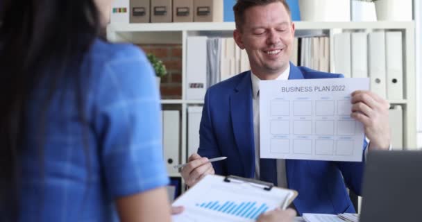 Uśmiechnięty lider płci męskiej pokazuje makietę kolegi do opracowania biznes planu na 2022 zwolniony film 4k - Materiał filmowy, wideo