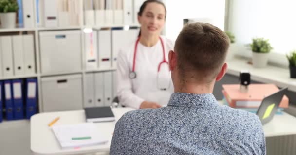 Jonge vrouwelijke arts praten met mannelijke patiënt in het kantoor van kliniek slow motion 4k film - Video