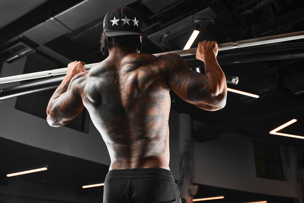 Erős és izmos sötét bőrű férfi edz modern felszereléssel a tornateremben. Portré izmos szivattyúzott fitness edző - Fotó, kép
