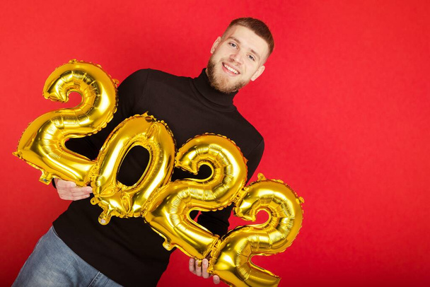 Portret van een man met de nummers 2022 op een rode achtergrond. Het komende nieuwe jaar - Foto, afbeelding