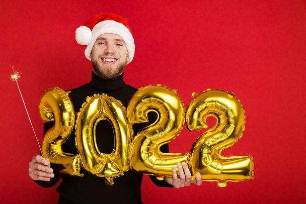 A man in a Santa Claus hat holds the numbers 2022 and a sparkler - Photo, Image