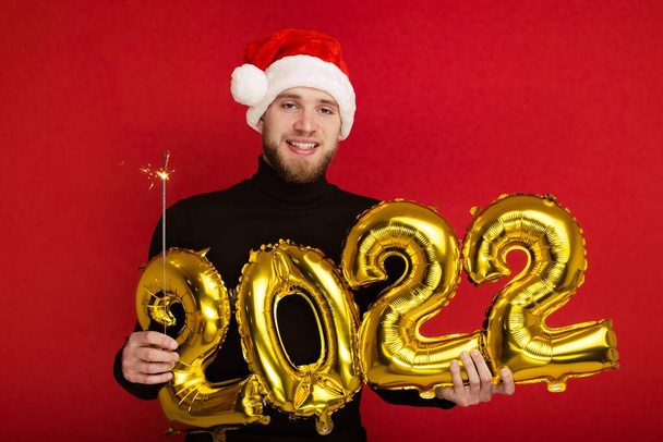 Człowiek w czapce Świętego Mikołaja trzyma numery 2022 i blask - Zdjęcie, obraz