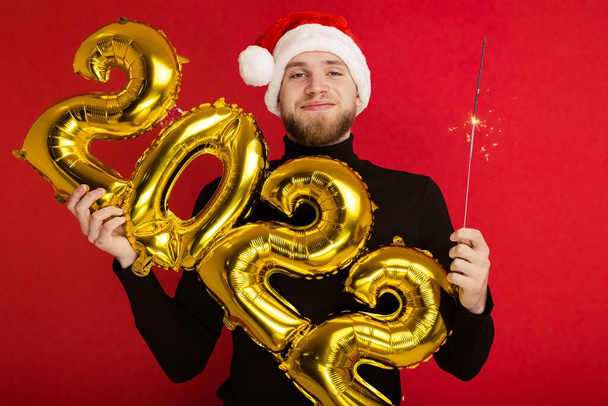 Человек в шляпе Санта-Клауса держит номера 2022 и искру - Фото, изображение