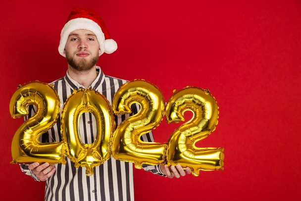 Ένας άντρας με χριστουγεννιάτικο καπέλο κρατάει τα νούμερα του 2022. Η Πρωτοχρονιά έρχεται σύντομα. - Φωτογραφία, εικόνα