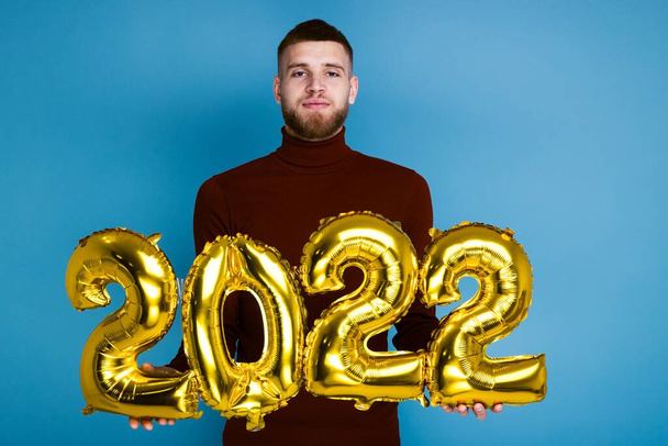 Un hombre sostiene los números 2022 de globos dorados. El próximo Año Nuevo - Foto, imagen