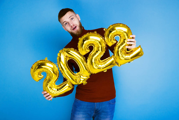 Ein Mann hält die Zahlen 2022 aus goldenen Luftballons. Das kommende neue Jahr - Foto, Bild
