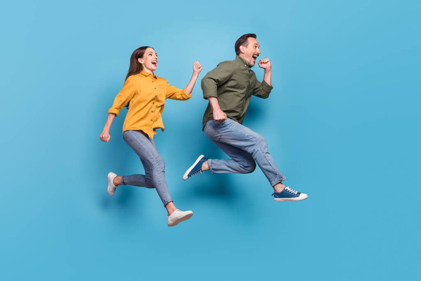Full length photo of brown haired husband wife jump up run empty space sale isolated on pastel blue color background - 写真・画像